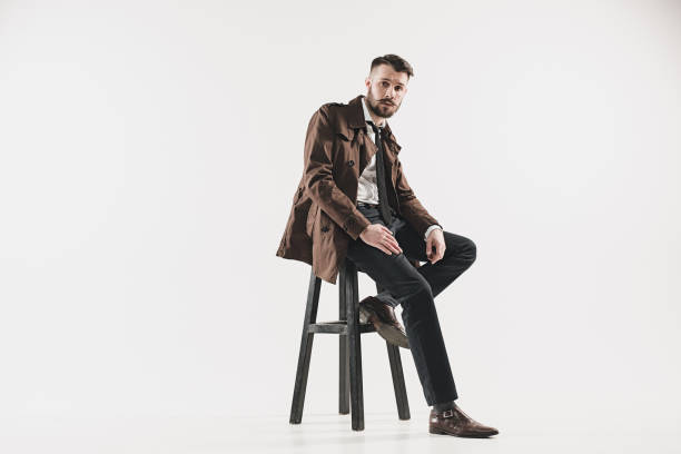 Portrait of stylish handsome young man sitting at studio against white. Man wearing jacket