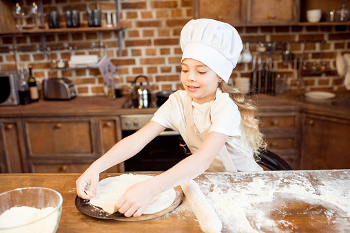 little girl making pizza dough on wooden tabletop in kitchen