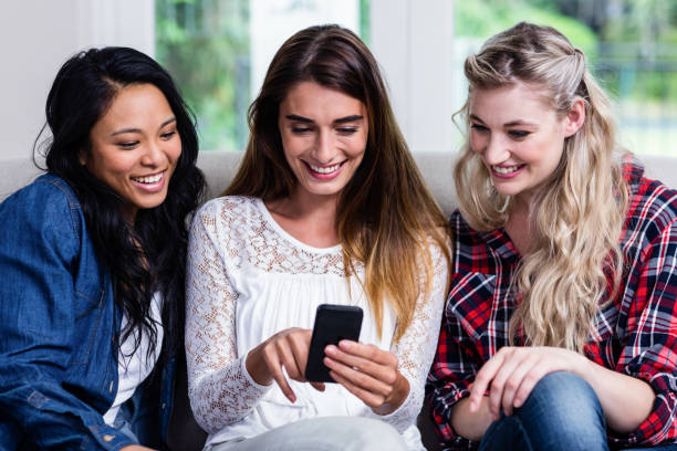 istock Female friends looking in mobile phone while sitting at home 673905620