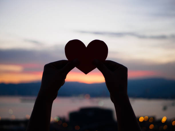 istock silhouette hand is raising the red paper heart with blur sunlight during sunset, 673933148
