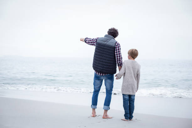 Rear view of father pointing while standing with son at sea shore