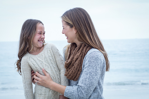 Close-up of cheerful mother and daughter at sea shore against sky