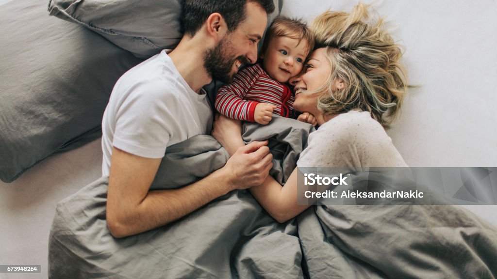 Morning routine with our baby boy Photo of young parents enjoying morning routine in a cosy bed with their baby boy Family Stock Photo