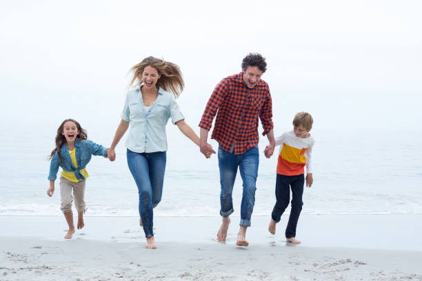 istock Happy family holding hands while running at sea shore 673961714