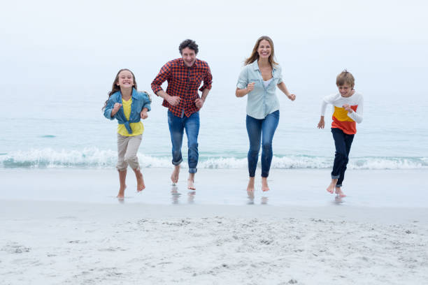istock Cheerful family running at beach against sky 673964126