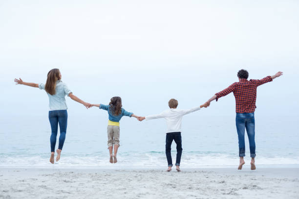 istock Family holding hands while jumping at sea shore 673964306