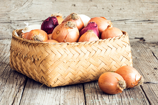 Raw onions in basket on wooden table