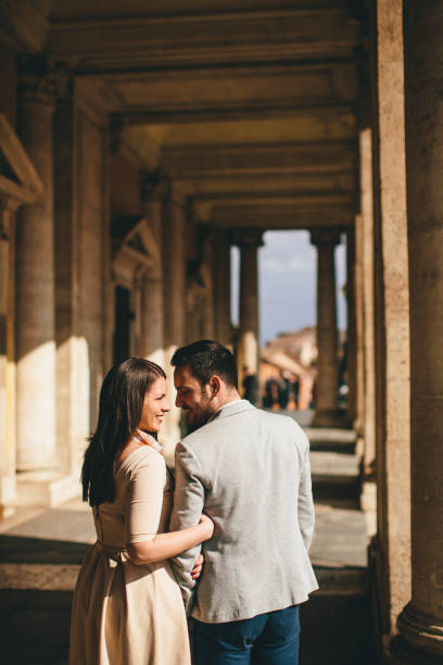 Female kissing male, walk near Baroque Roman Catholic church in Pidhirtsi, Lviv Ukraine. Couple stand on stairs near large columns of ancient temple at sunset. Woman hug man in nature autumn day.