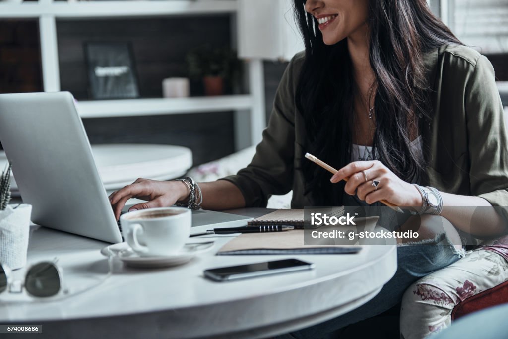 Busy day. Close-up of woman using laptop and smiling while sitting at her working place E-Learning Stock Photo