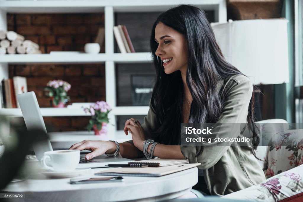 Concentrated at work. Beautiful young woman using laptop and looking at it while sitting at her working place E-Learning Stock Photo