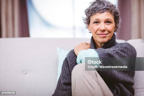Portrait Of Smiling Mature Woman Sitting On Sofa Stock Photo - Download Image Now - Women, One Woman Only, 50-59 Years