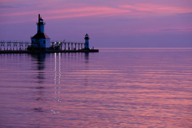 A lighthouse pier on Lake Michigan at sunset with pink clouds reflected in the water.  Sheboygan, Wisconsin, USA.
