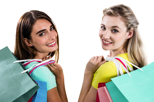 Portrait of smiling female friends holding shopping bags on white background