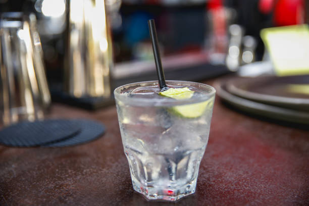 Vodka soda on a bar Close up vodka soda in a transparent glass, with a slice of lime and straw, placed on a bar. club soda stock pictures, royalty-free photos & images