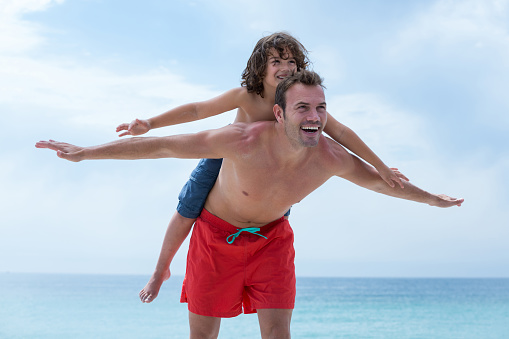 Man carrying son on back at sea shore against sky