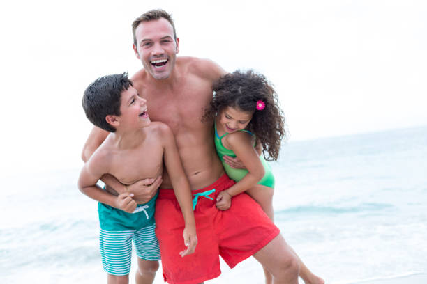 padre che porta bambini e si diverte in spiaggia - men beach running shirtless foto e immagini stock