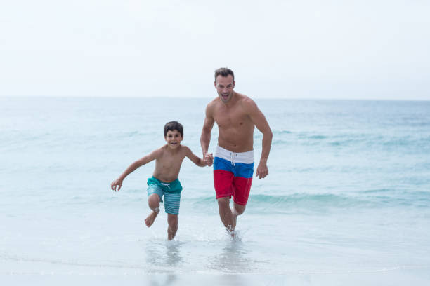 istock Full length of father and son running at beach 674083652