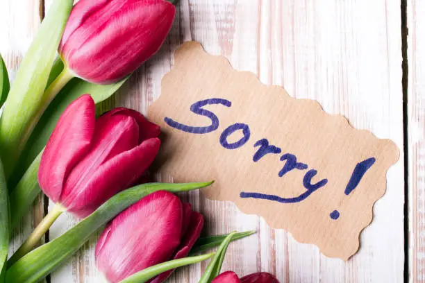 Photo of word SORRY and bouquet of tulips on wooden background