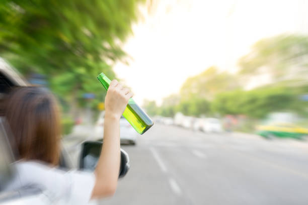 Drunk woman driving and holding beer bottle outside a car. stock photo