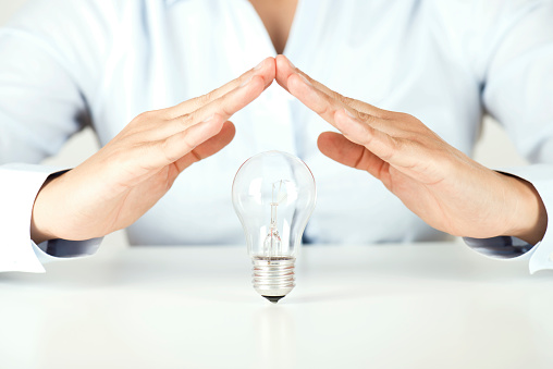 Businessperson is making a roof with hands to protect a light bulb representing an new idea.