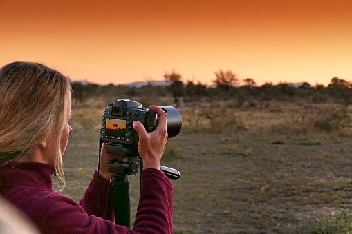 Tourist taking pictures with a digital camera mounted on a tripod during  a beautiful sunset.