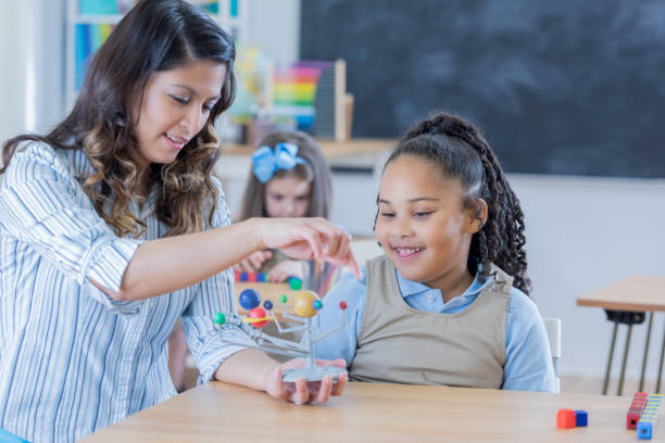 istock Cheerful teacher teaches young student about the solar system 674147138