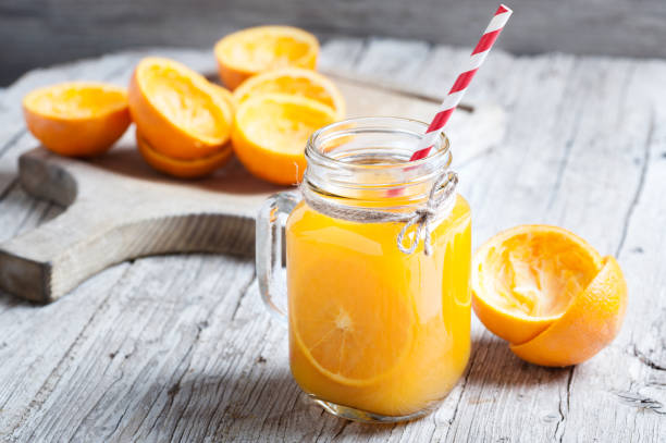 jugo de naranja exprimido en tarro de cristal con fondo rústico - freshly squeezed fotografías e imágenes de stock