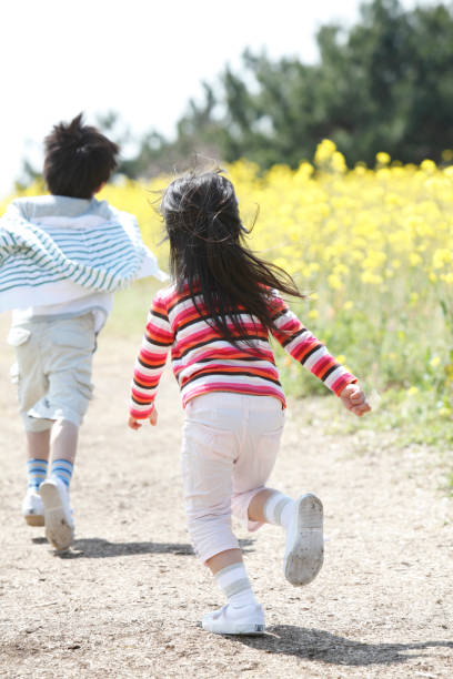 istock Rear view elementary school men and women running in rape field 674157560