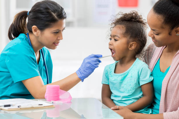 Pediatrician examines young patient Confident pediatrician examines a young female patient's throat. The doctor is using a tongue depressor. emergency medicine stock pictures, royalty-free photos & images