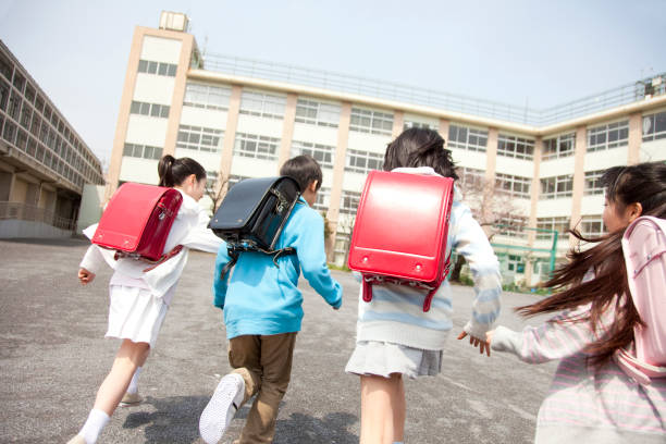 Vista posterior de los estudiantes de la escuela primaria van a la escuela cuatro - foto de stock