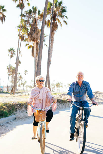 couple de personnes âgées actives en vélo - senior couple cycling beach bicycle photos et images de collection