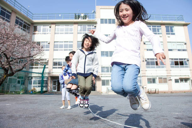 Schoolgirl in midair skipping with friends in school courtyard