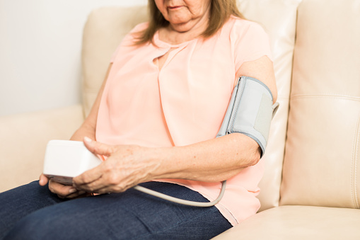 Retired Hispanic lady wearing digital tool to measure blood pressure range sitting at home