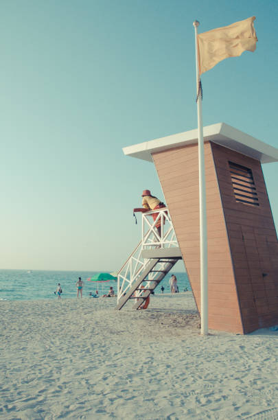 A lifeguard tower stands on a sandy beach, overlooking the ocean under a bright, cloudless sky