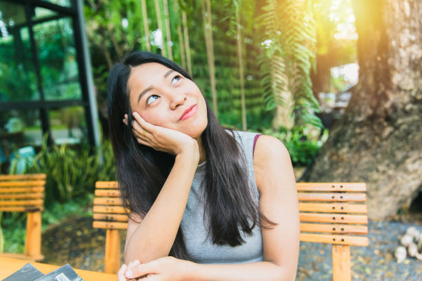 istock Thinking about or missing passed memory. Thai Asian women long hair hand chin rest and watching vision look out far away with sun light at cafe 674198564
