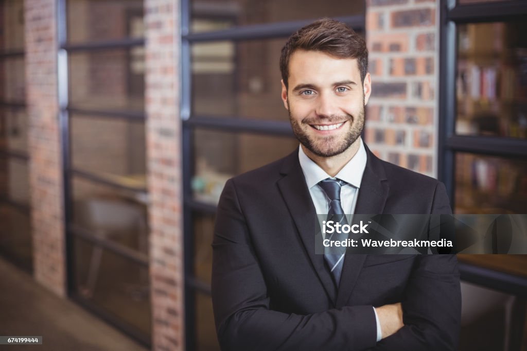 Handsome businessman with arms crossed standing in office Portrait of happy handsome businessman with arms crossed standing in office Suit Stock Photo