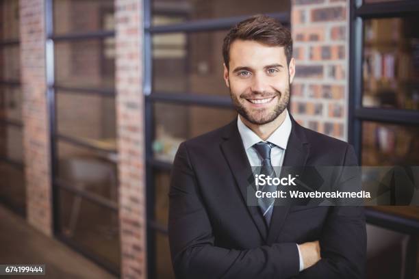 Handsome Businessman With Arms Crossed Standing In Office Stock Photo - Download Image Now