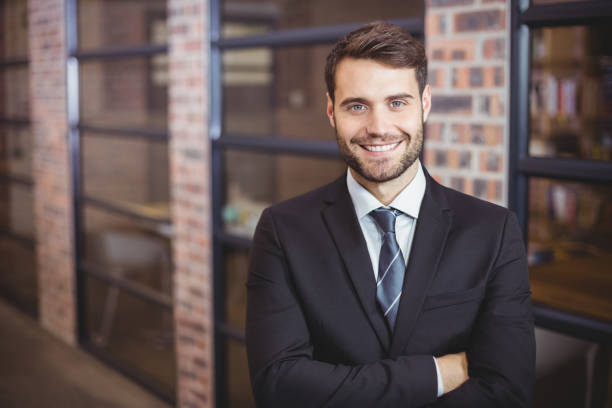 handsome businessman with arms crossed standing in office - mans suit imagens e fotografias de stock