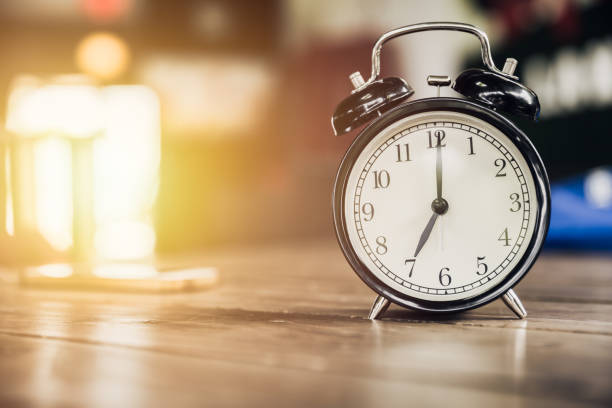 istock 7 o'clock time retro clock on wood table with sun light background 674203194