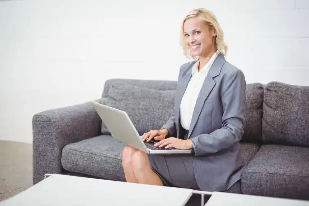 Portrait of smiling bussinesswoman working on laptop while sitting on sofa at office