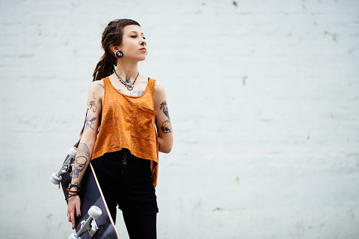 Portrait of hipster - punker young woman with tattoos and dreadlocks, piercings and jewelry. Unique beautiful young woman living alternative life, but still typical for millennial generation people. Young woman is going to skate park