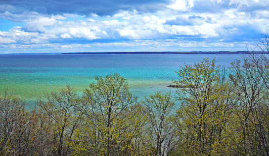 New spring-green leaves on the trees and a backdrop of the Caribbean-colored waters of West Grand Traverse Bay near Suttons Bay, Michigan.