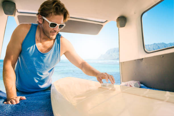 A man getting ready to go surfing waxing his board out of his campervan.