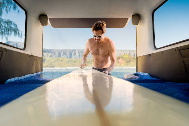 A man getting ready to go surfing waxing his board out of his campervan.