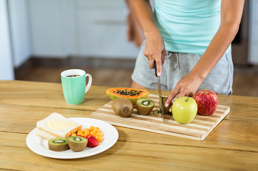 Midsection of young woman cutting fruits at kitchen counter