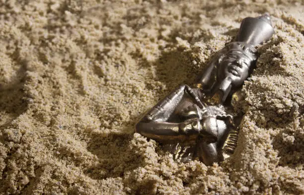 Photo of Pharaoh metal statuette laying in sand.