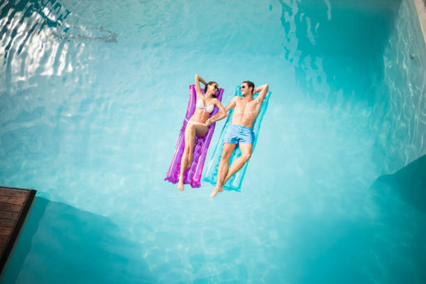 Happy couple relaxing on inflatable raft at swimming pool stock photo