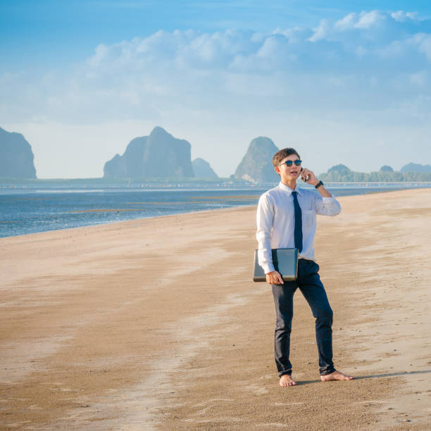 istock Relaxing Businessman using  laptop and smartphone on the beach 674388172