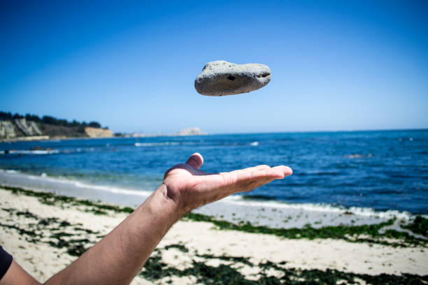 jogando uma pedra. fundo de praia - throwing stone human hand rock - fotografias e filmes do acervo
