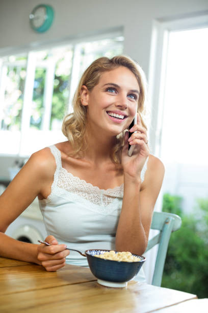 istock Young woman talking on mobile phone while having breakfast at home 674396810